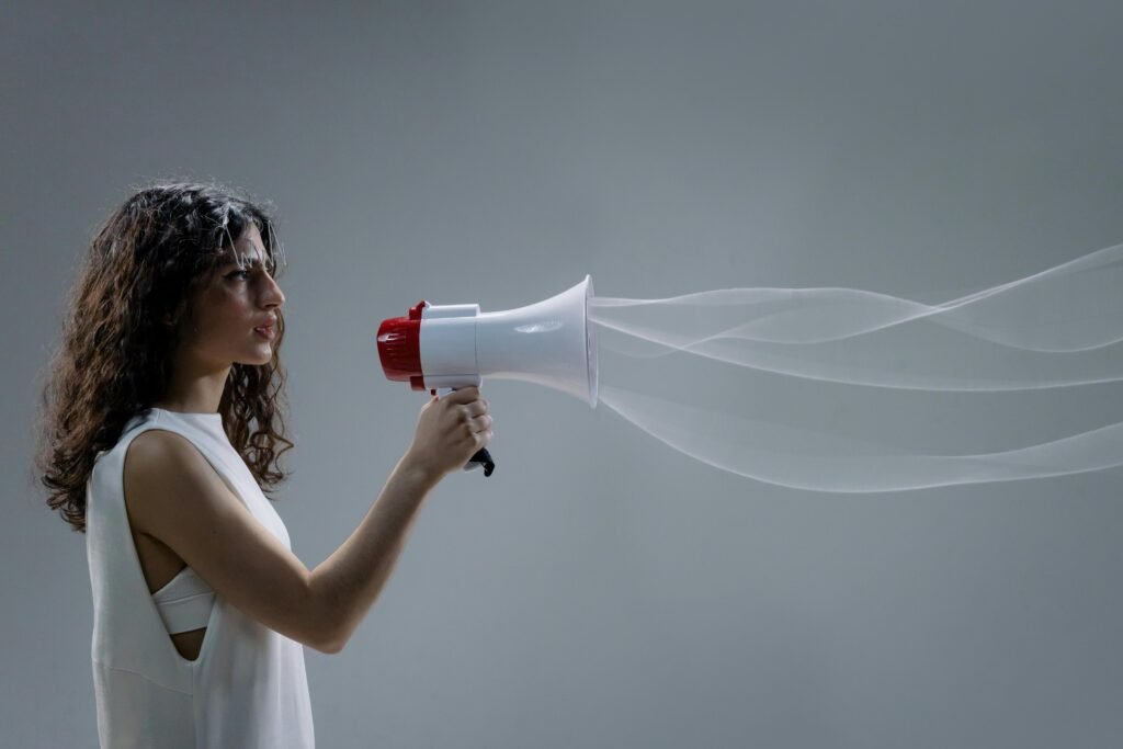 Woman using a megaphone emitting sound waves on a gray background.